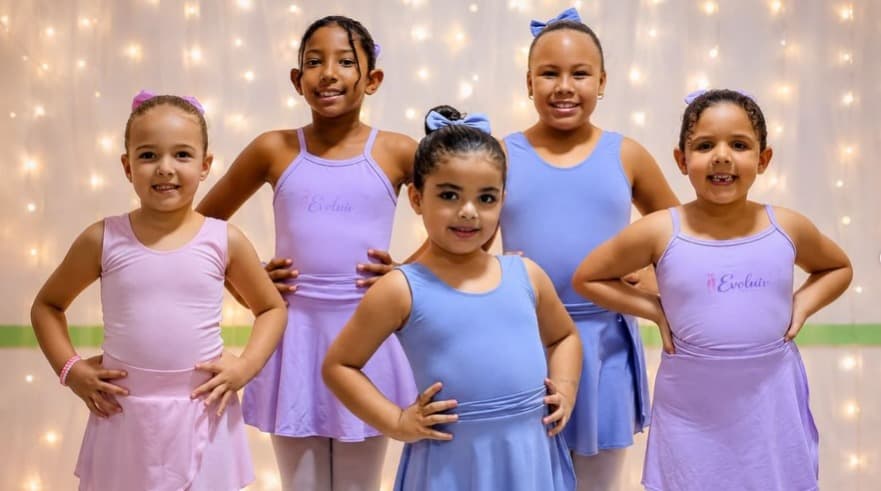 Cinco alunas de collant rosa, lilás e azul posando juntas na aula de dança